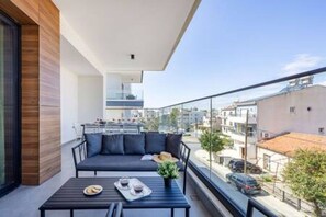 En balkon med en sofa, et bord med bakke og udsigt over byen.