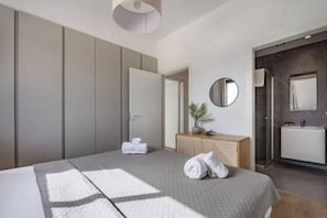 A modern hotel room with a bed, a bedside table, a mirror, and a bathroom with a sink and shower.