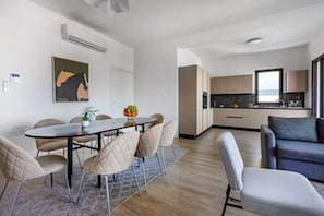 A modern living room with a sofa, a dining table with chairs, and a kitchen area with cabinets and a window.