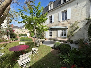 Un bâtiment en pierre doté d’un patio avec jardin, d’une table et de chaises, et d’un arbre.