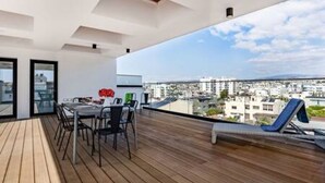 Ein Balkon mit Esstisch und Stühlen, einer Liege und Blick auf die Stadt.