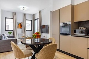 Een moderne woonkamer met een eettafel, stoelen, een flatscreen-televisie en een keukenhoek met een magnetron.