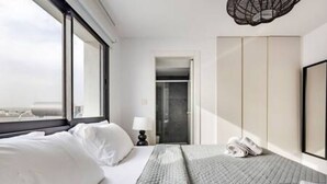 Habitación de hotel con cama, escritorio, silla, armario y vistas a la ciudad.
