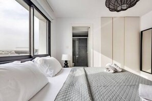Ein Hotelzimmer mit Bett, Schreibtisch, Stuhl, Kleiderschrank und Blick auf die Stadt.
