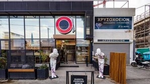 Un edificio moderno con fachada de vidrio, un letrero circular rojo y blanco, y una señal que indica espacios de estacionamiento para huéspedes.