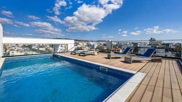 Una piscina en la azotea con sillas de descanso y vistas de la ciudad.
