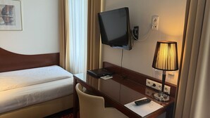 A hotel room with a bed, desk, chair, television, lamp, and a wall-mounted power outlet. - Hotel Jäger Single Room with Balcony (Wien)