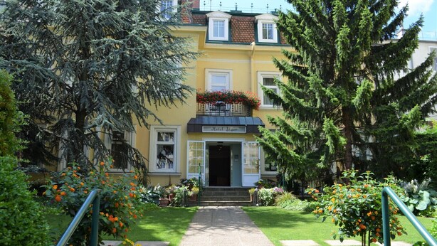 A yellow building with a balcony, a garden with flowers, and a clear sky. - Hotel Jäger Single Room with Balcony (Wien)