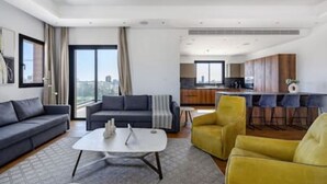 Un salon moderne comprenant un canapé, des fauteuils, une table basse et un coin cuisine avec des tabourets de bar.