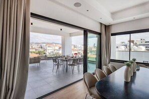 Ein modernes Hotelzimmer mit großem Fenster, einem Essbereich mit Stühlen und Tisch sowie Blick auf die Stadtlandschaft.
