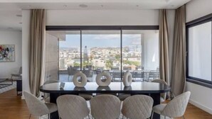 Une salle à manger moderne avec une grande table ronde, six chaises et une vue sur le paysage urbain grâce à de grandes fenêtres.