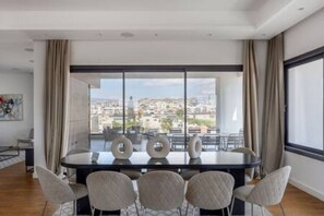 Ein moderner Essraum mit einem großen runden Tisch, sechs Stühlen und Blick auf eine Stadtkulisse durch große Fenster.