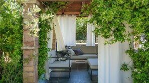 Ein Sitzbereich im Freien mit einer Couch und einem Tisch, umgeben von Grünpflanzen und einer Pergola.
