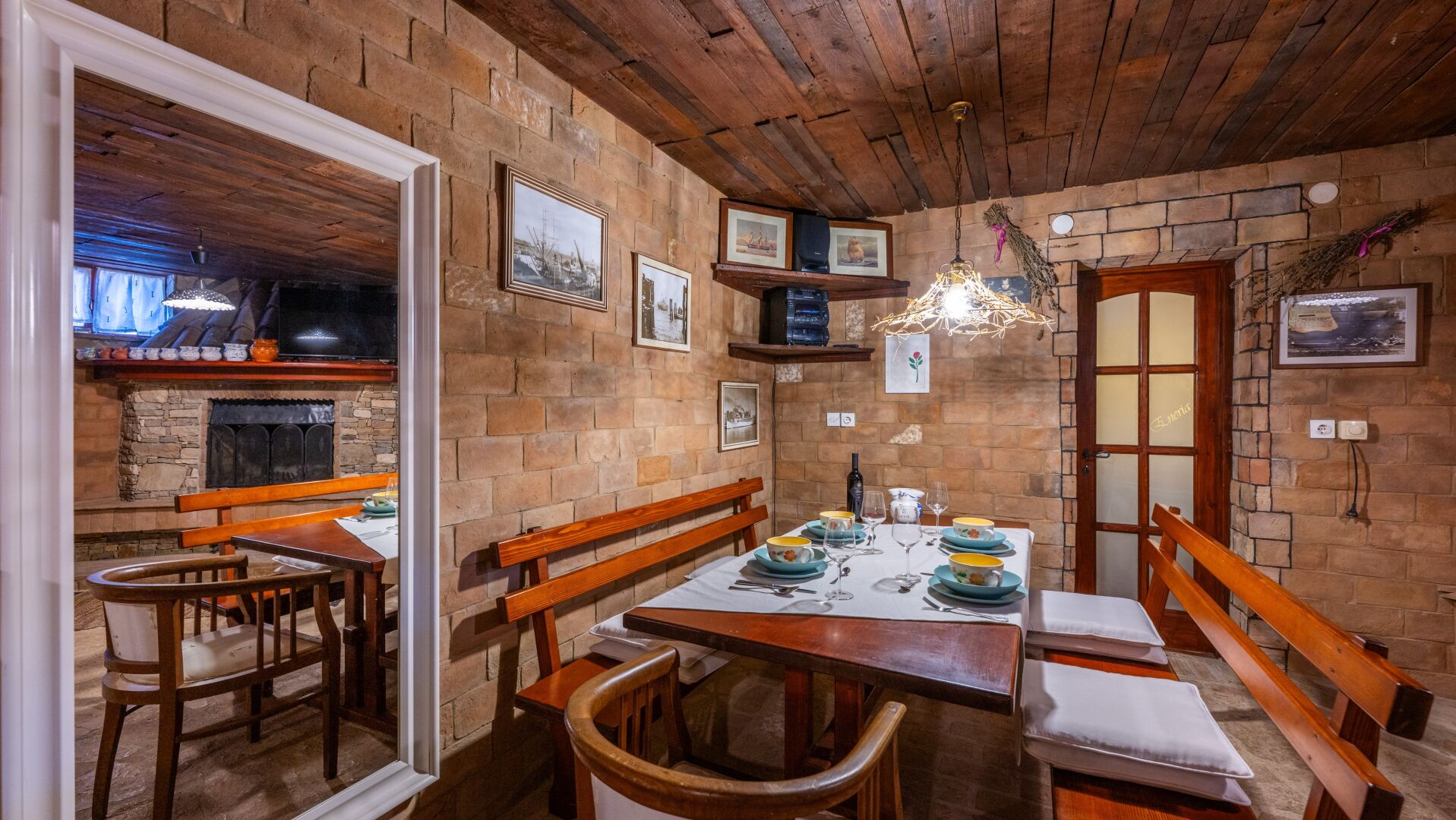 Zona de menjador rústica amb bancs de fusta i taula preparada per a dues persones, amb paret de pedra i sostre de fusta.
