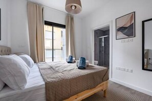 Un dormitorio con cama, ventana con cortinas, zona de ducha y una obra de arte colgada en la pared.