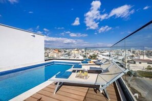 Una piscina en la azotea con sillones de descanso y una mesa, con vistas a un paisaje urbano.