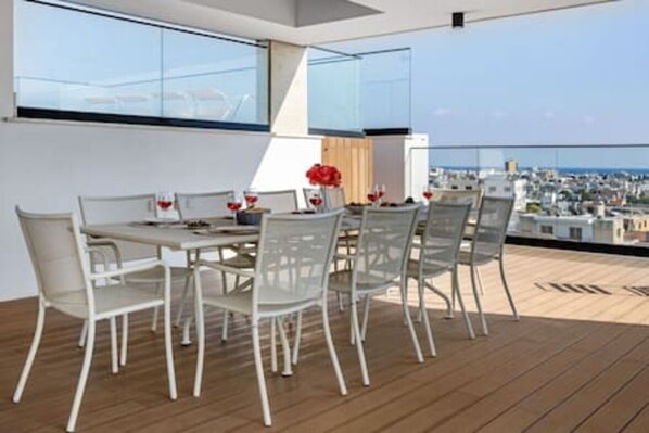Una terraza en la azotea con una mesa y sillas, vista panorámica de la ciudad y suelo de madera.