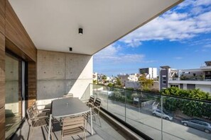 Un balcón con mesa y sillas, una vista despejada de la calle y una fachada de edificio moderna.