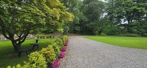 Ein Kiesweg schlängelt sich durch einen gepflegten Garten mit Bank und Stühlen, umgeben von üppiger Bepflanzung und blühenden Pflanzen.