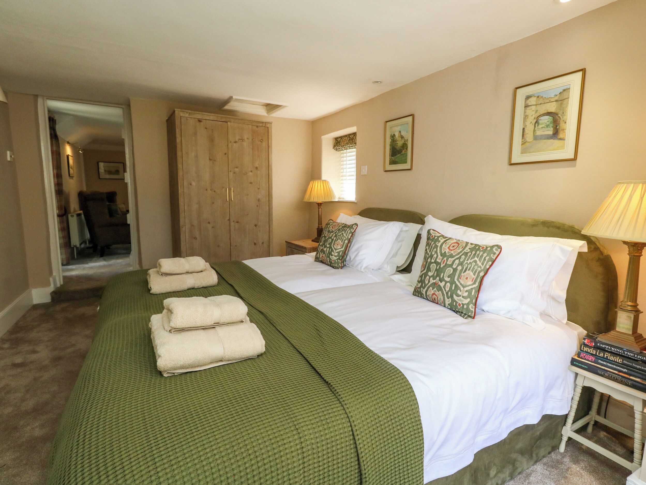 A double bed with green bedding, two pillows, a bedside table with a lamp, and a wooden wardrobe.