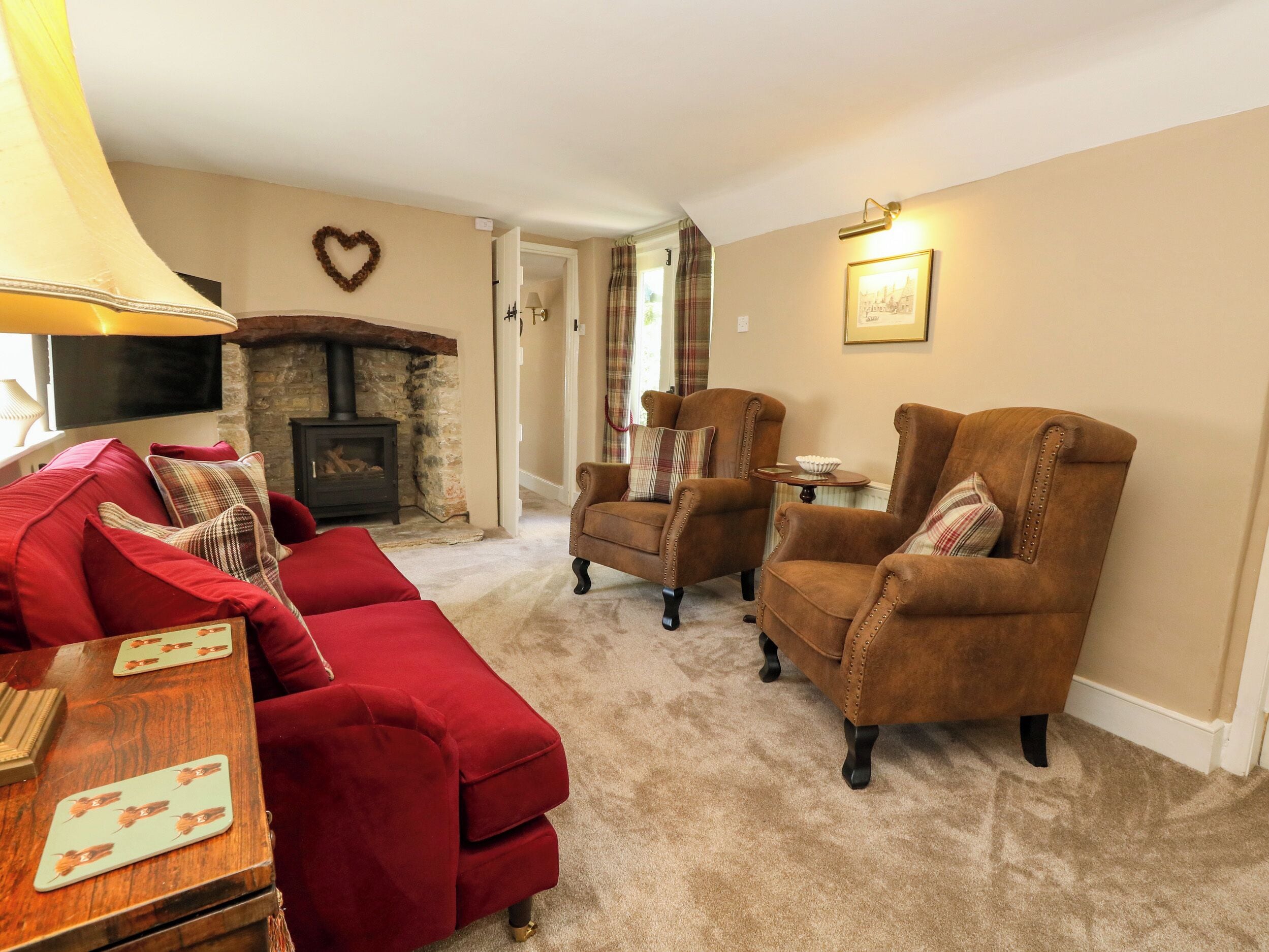 A cozy living room with a red sofa, two brown armchairs, a fireplace, and a television.
