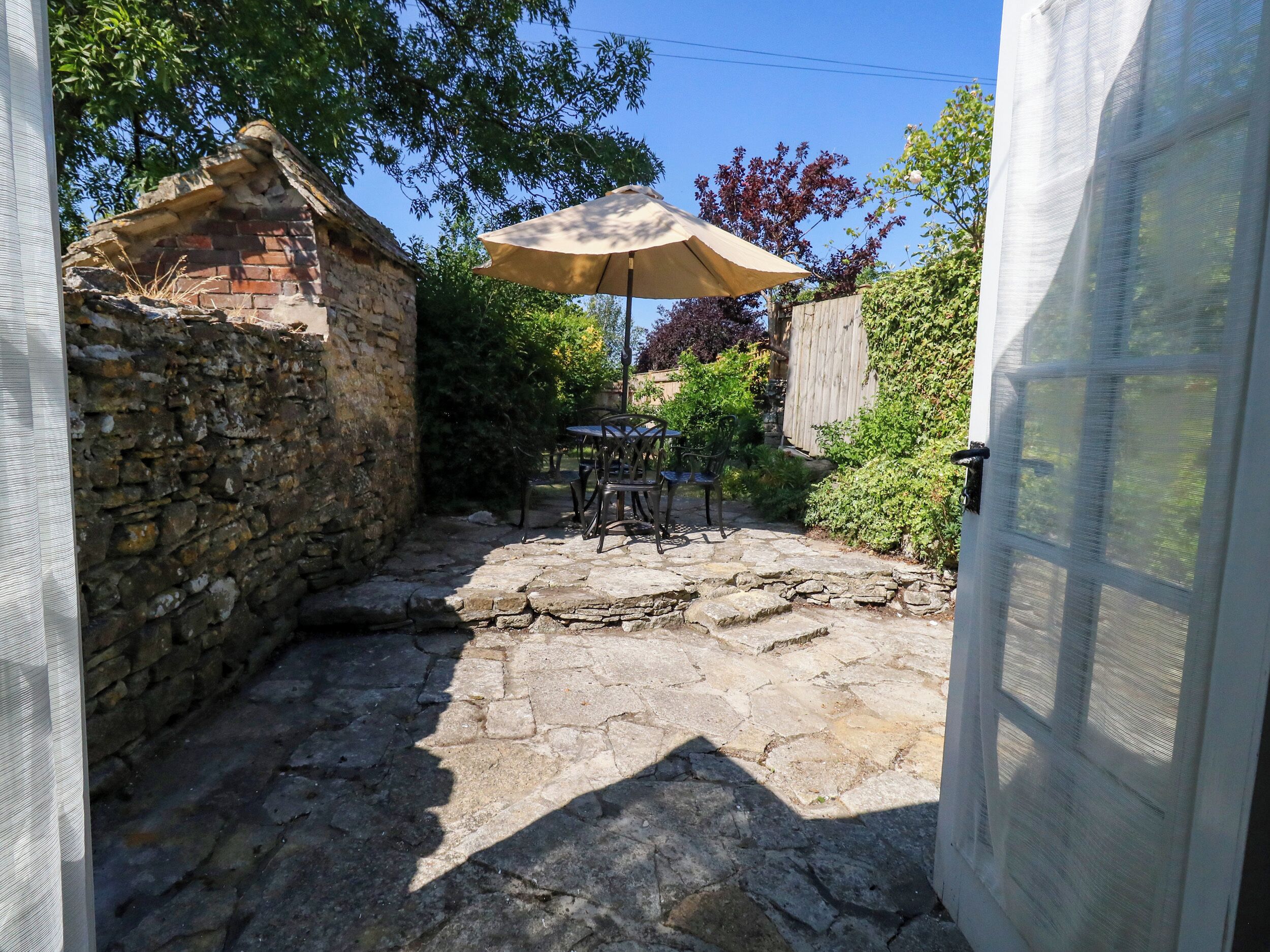 Un patio de piedra con una mesa y sillas, una puerta parcialmente visible y un muro de ladrillo.