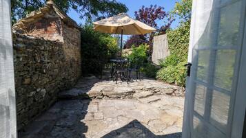 Un patio de piedra con una mesa y sillas, una puerta parcialmente visible y un muro de ladrillo.