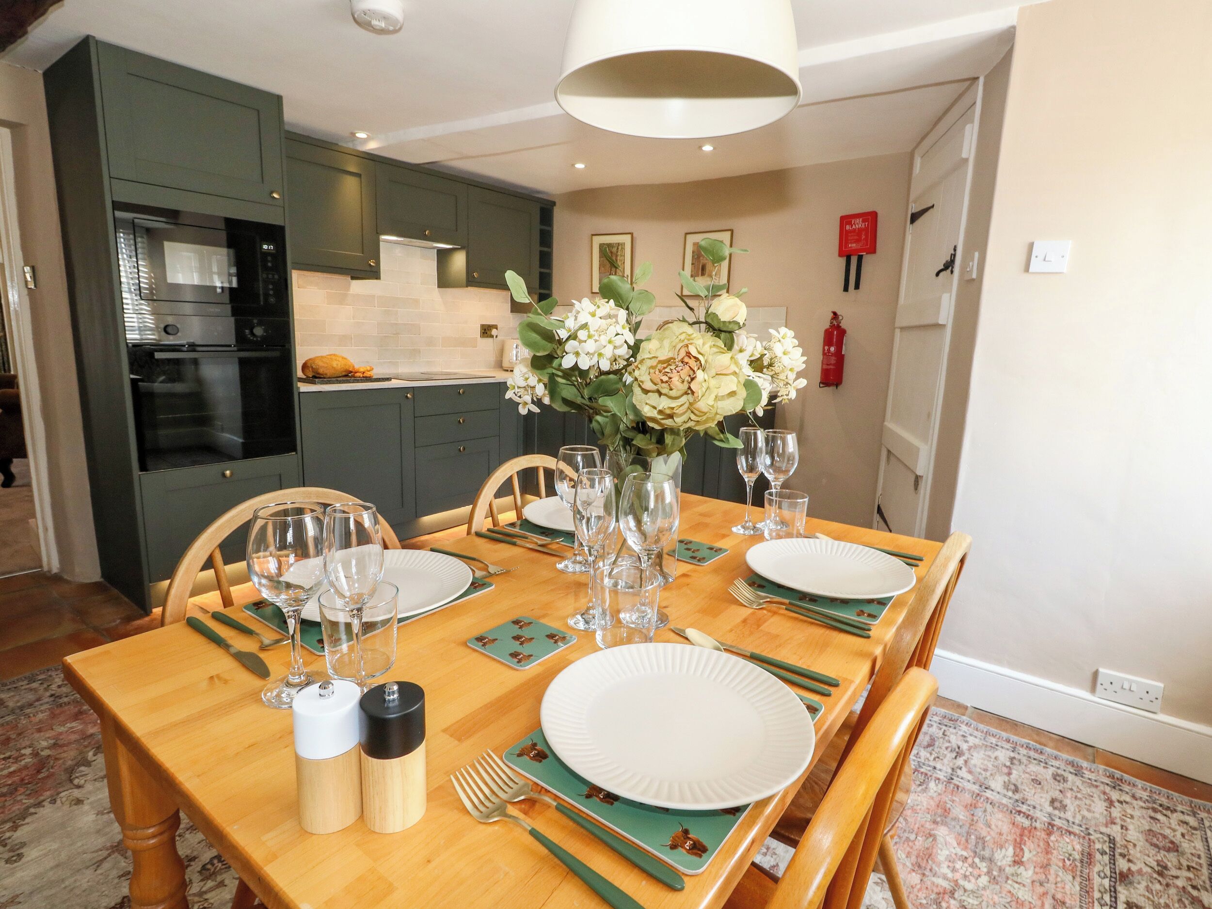 A dining area with a wooden table set for six, including plates, glasses, cutlery, and a vase with flowers.
