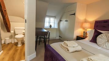 Un dormitorio con cama, mesita de noche, lámpara y ventana con persianas.