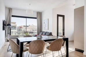 Una habitación de hotel moderna con comedor, ventanas grandes y vistas a la ciudad.