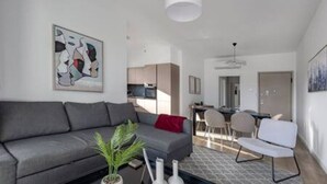 A modern living room with a grey sofa, a coffee table with a plant, and a dining area in the background. - 101 Piliou City View & Shared Rooftop Pool (Limassol)