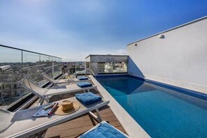 Piscina en la azotea con sillas de descanso y barandilla de cristal.