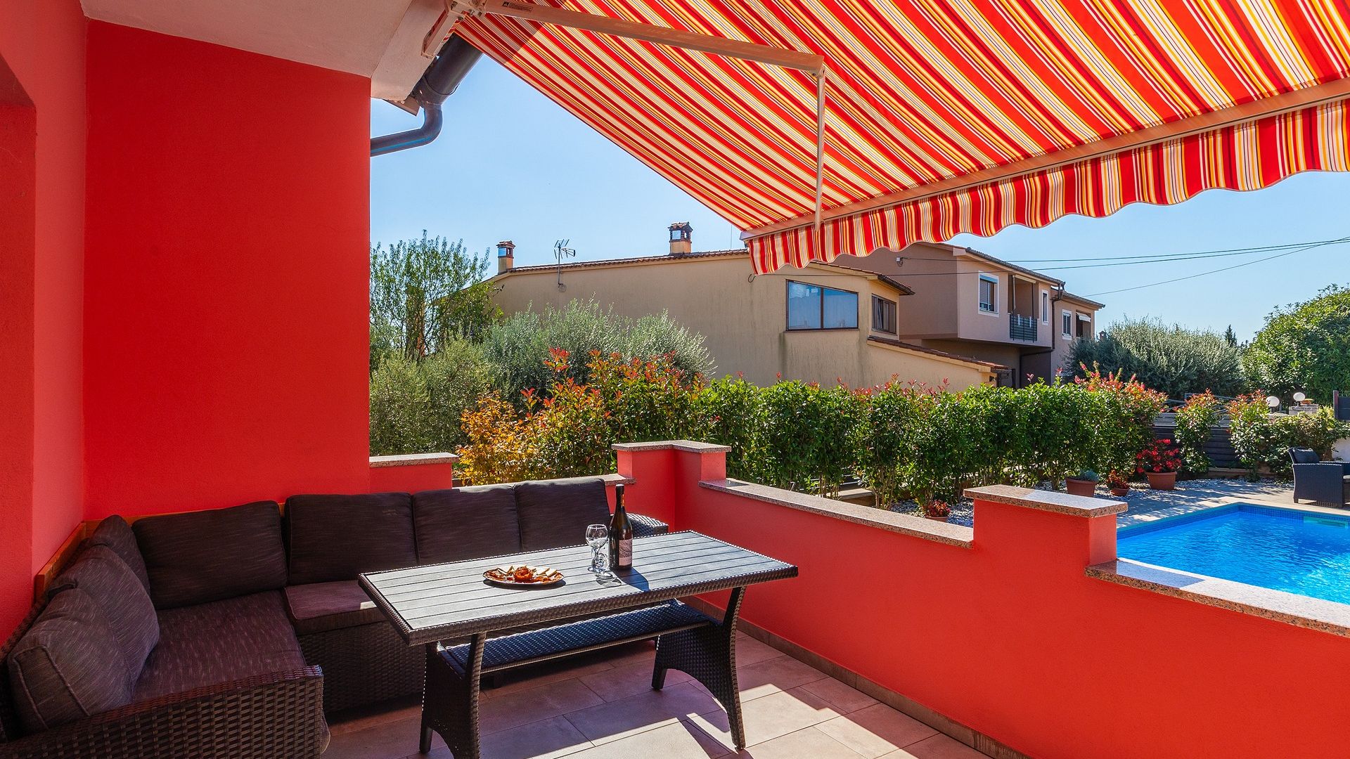 Un espace extérieur aux murs rouges, avec une piscine, une table sur laquelle se trouve une bouteille et un canapé.