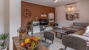 Ein modernes Wohnzimmer mit Fernseher, Sofa, Couchtisch und Obstschale.