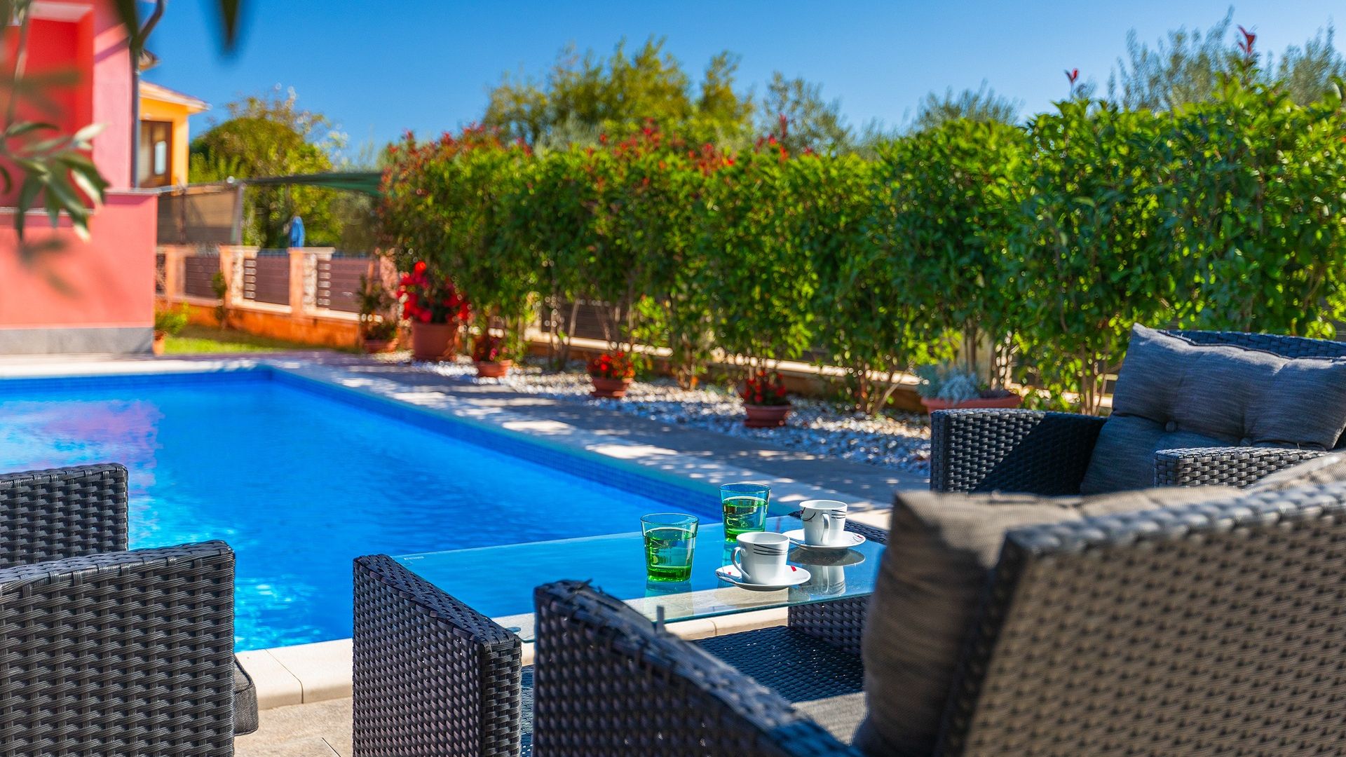 Un espace aménagé au bord de la piscine, avec des meubles en osier et une table où sont servis des boissons.