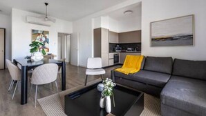A modern living room with a sofa, a coffee table with a vase, and a dining area with chairs and a table. - 202 Piliou Large Balcony & Shared Rooftop Pool (Limassol)