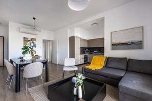A modern living room with a sofa, a coffee table with a vase, and a dining area with chairs and a table. - 202 Piliou Large Balcony & Shared Rooftop Pool (Limassol)