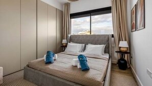 A hotel room with a bed, a window, a lamp, and a wall-mounted artwork. - 202 Piliou Large Balcony & Shared Rooftop Pool (Limassol)