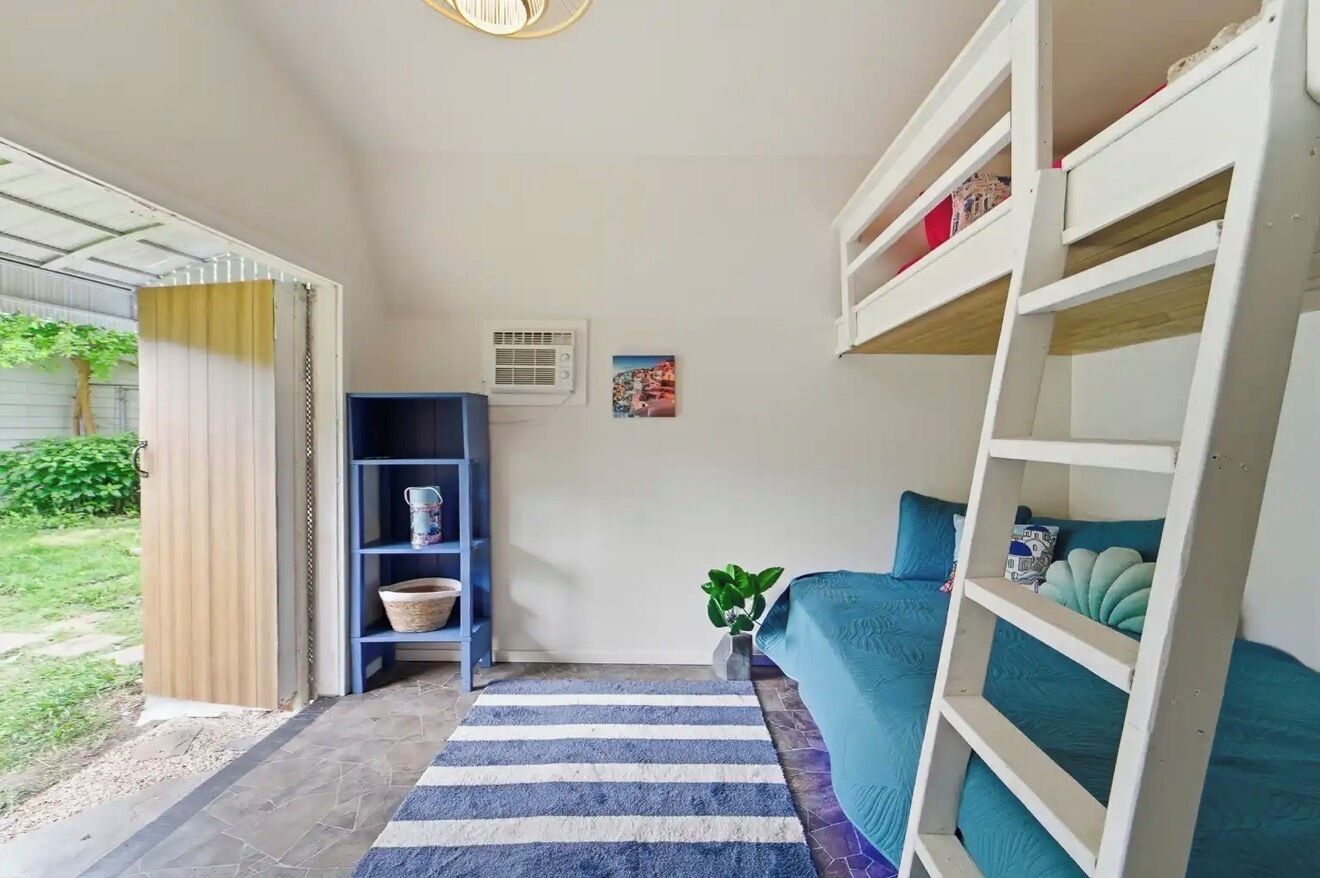 Een kamer met een stapelbed, een blauwe bank, een gestreept vloerkleed, een boekenkast en een kleine plant.