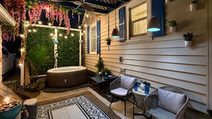 A cozy outdoor patio with a hot tub, seating area, and string lights.