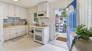 A kitchen with white cabinets, a microwave, and an oven. There is a door leading to an outdoor area with a blue door and a potted plant.