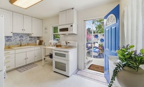 A kitchen with white cabinets, a microwave, an oven, and a blue door leading outside.