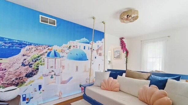 A room with a mural of a coastal scene, a bed with blue and beige bedding, and a wooden floor.