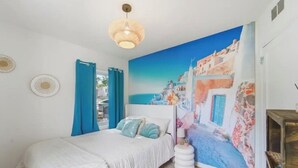 A bedroom with a bed, a wall mural, a hanging light fixture, and a small white table.