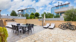 Eine Terrasse mit Tisch und Stühlen, Liegestühlen und Fahrrädern.