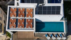 Un bâtiment moderne doté d’une piscine sur le toit, de panneaux solaires et d’une terrasse en bois.