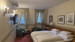 Een hotelkamer met een groot bed, twee stoelen, een bureau, een lamp en twee ramen met gordijnen.