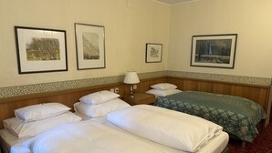 Hotelkamer met twee bedden, een nachtkastje, een lamp en drie ingelijste foto’s aan de muur.