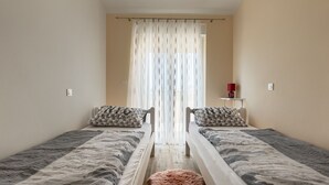 Quarto com duas camas, cortina, abajur vermelho e uma pequena mesa.