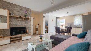 Uma sala de estar moderna com uma televisão de tela plana, uma mesa de centro de vidro e um sofá com almofadas.